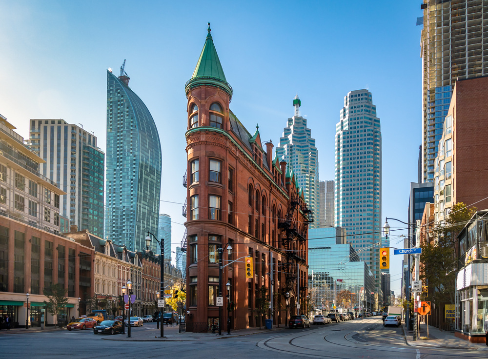 Ceglany budynek Gooderham z zieloną wieżyczką na tle nowoczesnych wieżowców w centrum Toronto.