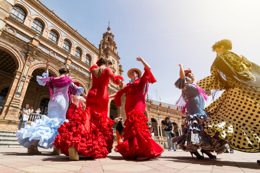 Kobiety w czerwonej i żółtej sukni tańczące flamenco na Plaza de España w Sewilli.