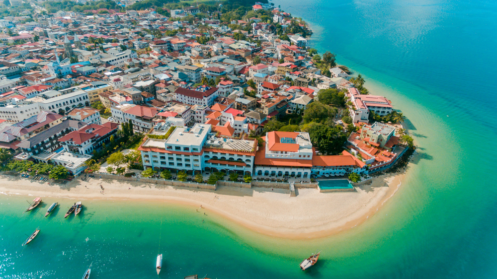 Historyczna zabudowa Stone Town na Zanzibarze oraz plaża i łodzie przy nabrzeżu, widok z lotu ptaka.