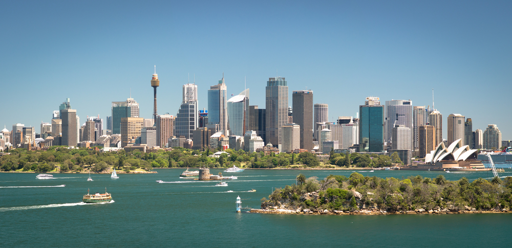 Panorama Sydney nad zatoką, z miejskimi wieżowcami, łodziami i Sydney Opera House.