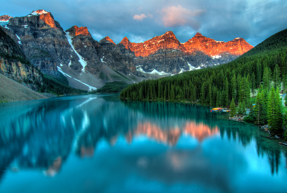 Oświetlone wschodzącym słońcem szczyty Gór Skalistych odbijające się w jeziorze Moraine w Parku Narodowym Banff.