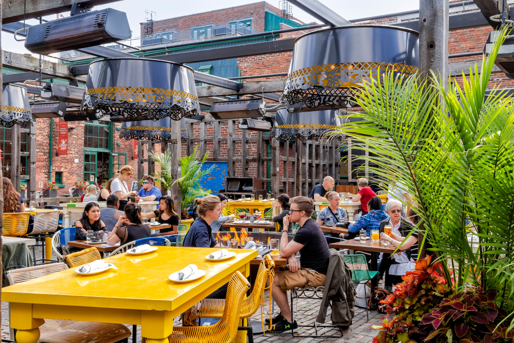 Goście przy stołach restauracyjnego ogródka wśród ceglanej zabudowy Distillery District w Toronto.
