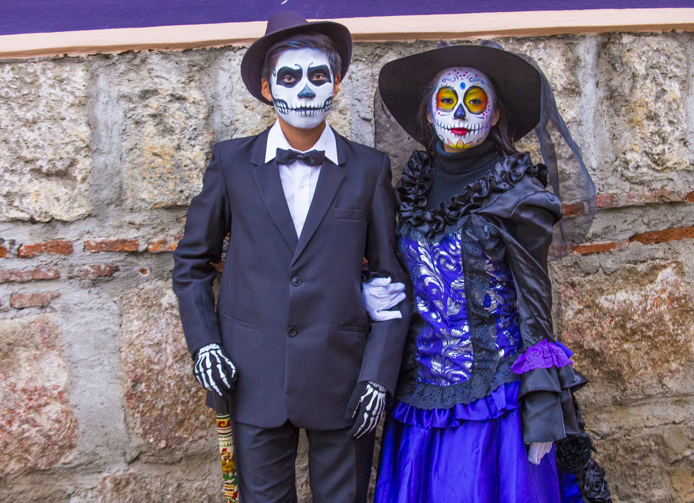 Dwie osoby podczas obchodów Día de Muertos w Oaxaca, w odświętnych strojach i makijażu przypominającym czaszki.