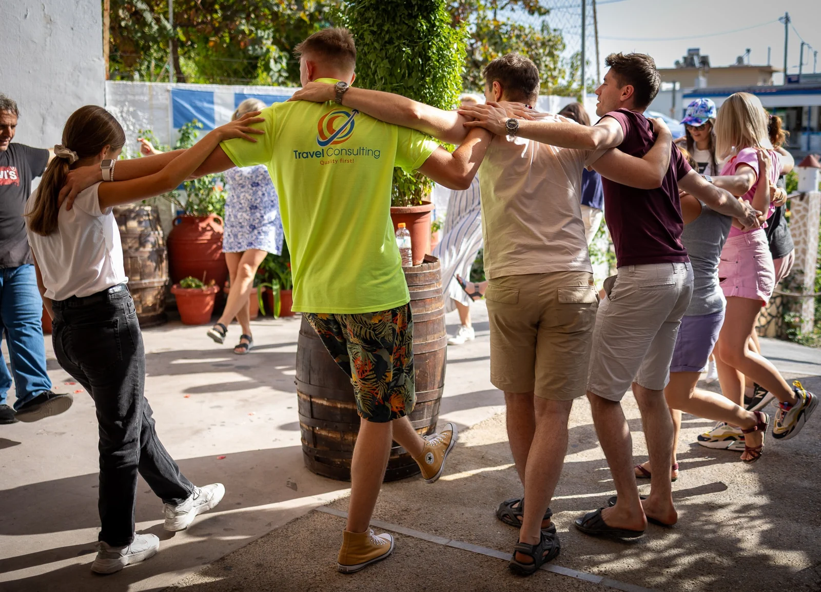 Uczestnicy wyjazdu na Rodos tańczą w kręgu z członkiem zespołu Travel Consulting