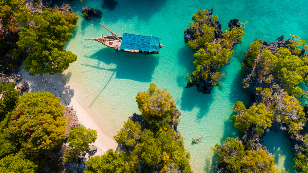 Łódź w turkusowej wodzie przy zielonych wysepkach i piaszczystej plaży w okolicy Pamundy na Zanzibarze, widok z góry.