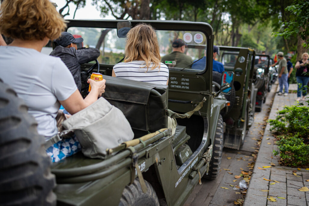 Uczestnicy podróżują otwartymi terenówkami po ulicy Hanoi.