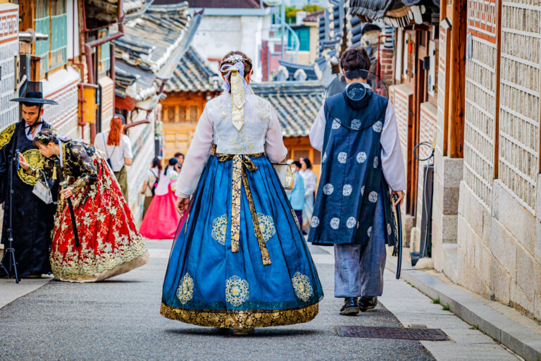 Osoby w strojach hanbok na ulicy wśród tradycyjnych koreańskich domów w Seulu.