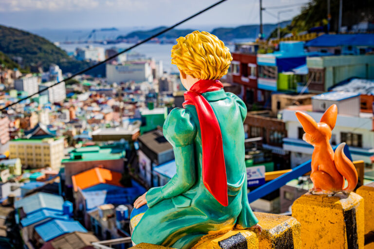 Figury Małego Księcia i lisa na tle kolorowych domów Gamcheon Culture Village w Busan.