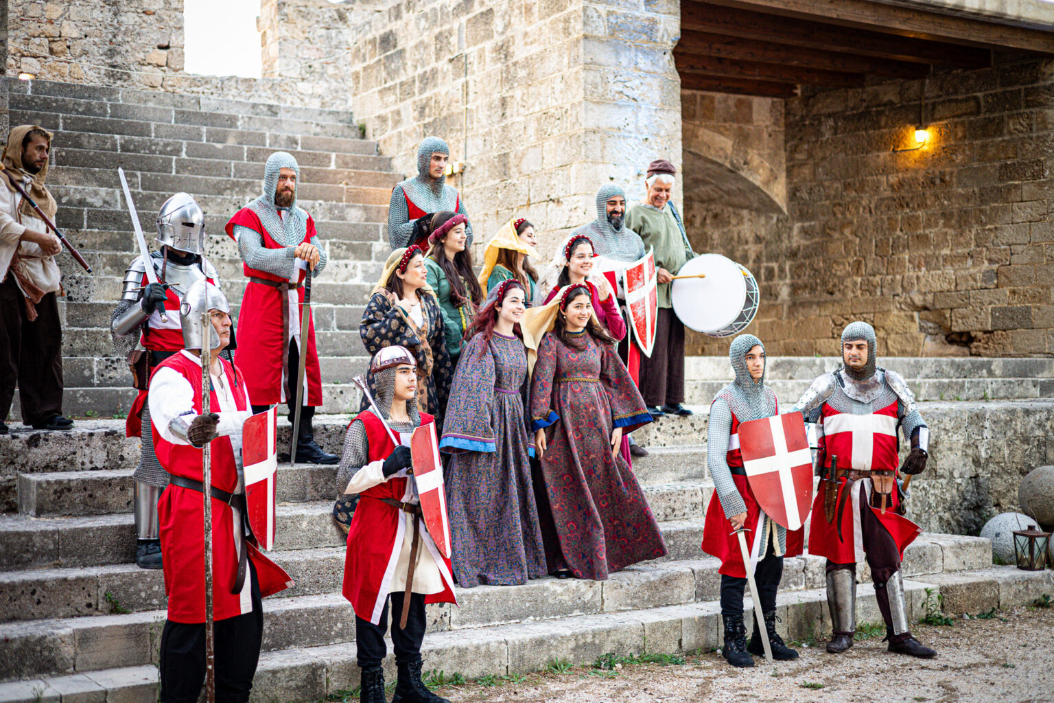 Aktorzy w historycznych kostiumach rycerzy i mieszczan na kamiennych schodach starego miasta Rodos.