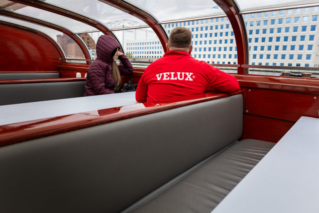 Uczestnik w czerwonej koszulce z napisem VELUX podczas rejsu łodzią po Kopenhadze.