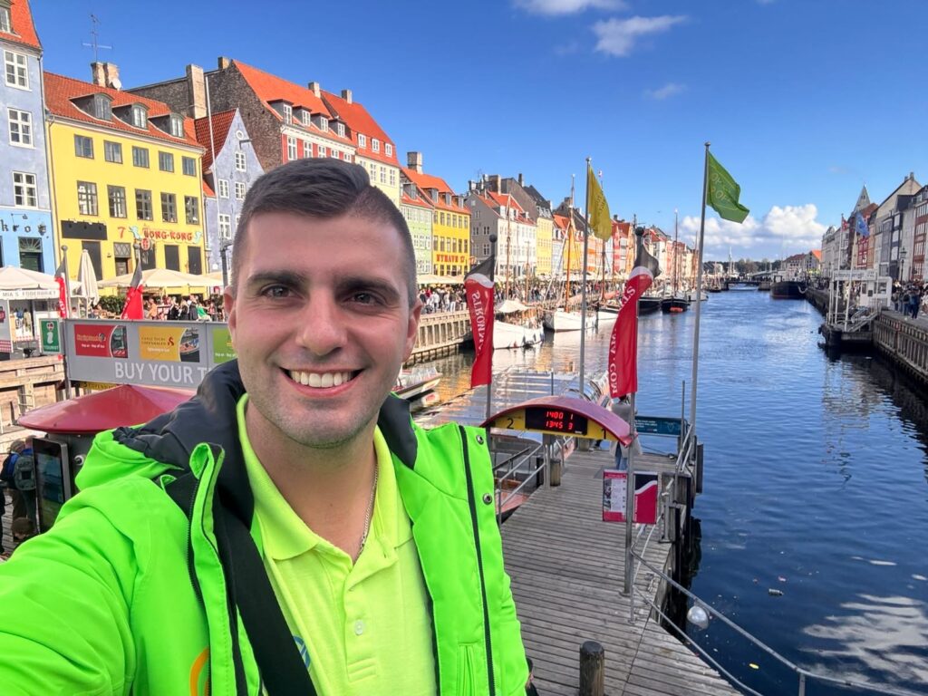 Uśmiechnięty mężczyzna na łodzi przy kolorowych kamienicach Nyhavn w Kopenhadze.